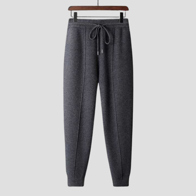 Pantalon de jogging gris foncé en laine, suspendu sur un cintre en bois, avec cordon de serrage, idéal pour confort et style décontracté.