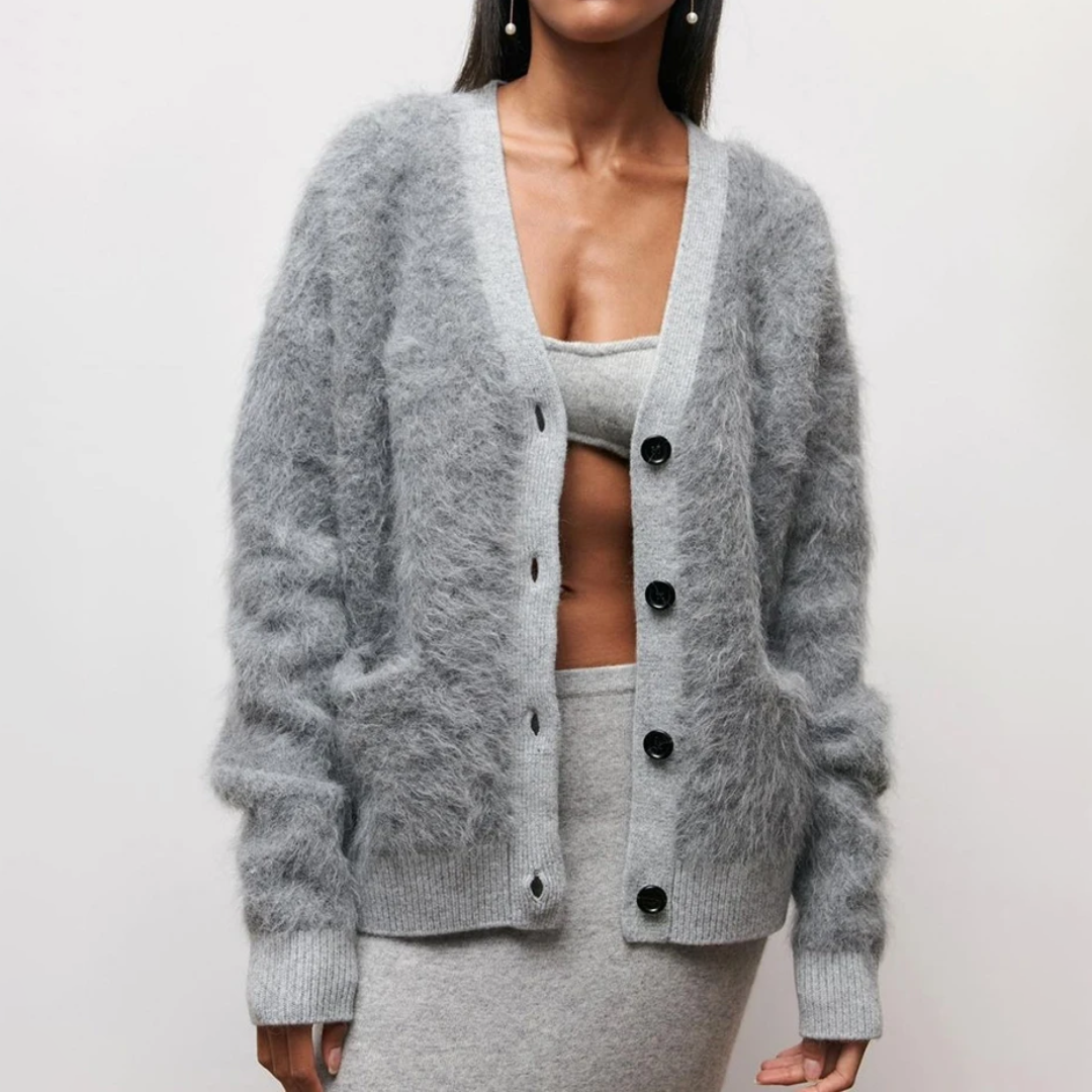 Femme portant un cardigan gris en mohair avec boutons noirs, assorti à une jupe et un haut gris. Mode automne-hiver, tenue élégante et confortable.
