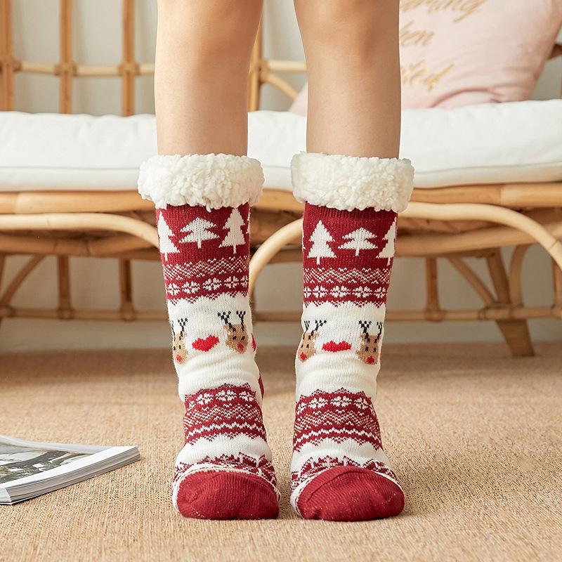 Chaussettes de Noël rouges et blanches avec motifs rennes et sapins, portées sur un tapis beige, ambiance cosy et festive.