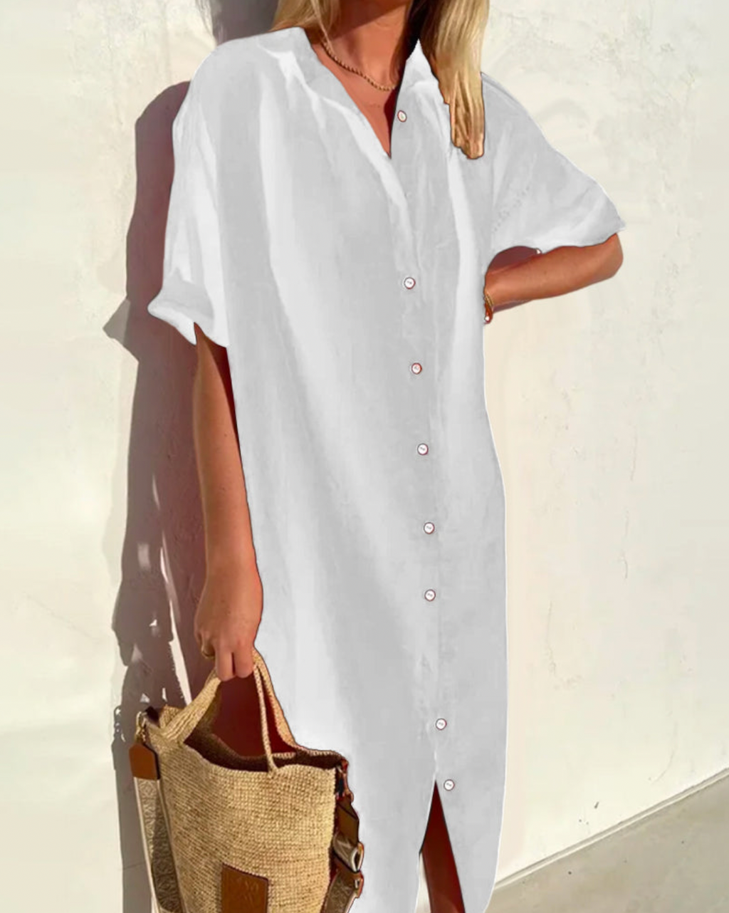 Robe chemise blanche en lin portée par une femme, manches courtes, avec sac en paille. Mode estivale élégante et décontractée.