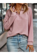 Femme portant un pull rose texturé à col zippé et un jean bleu clair, accessoirisée d'un collier doré, marchant en ville. Mode automne décontractée.
