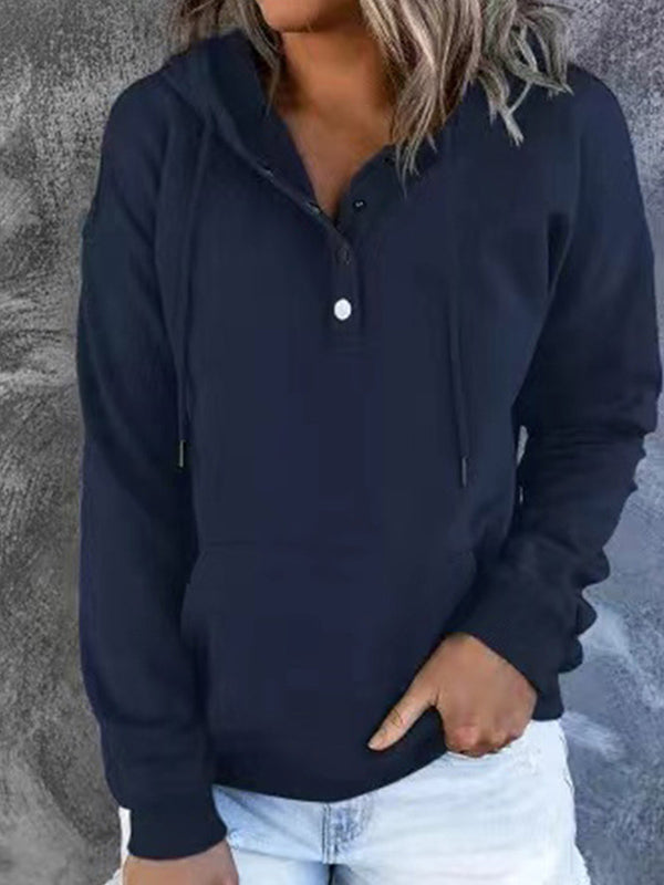 Femme portant un sweat à capuche noir avec boutons, manches longues, devant un mur gris. Mode décontractée, tenue automne-hiver, style urbain.