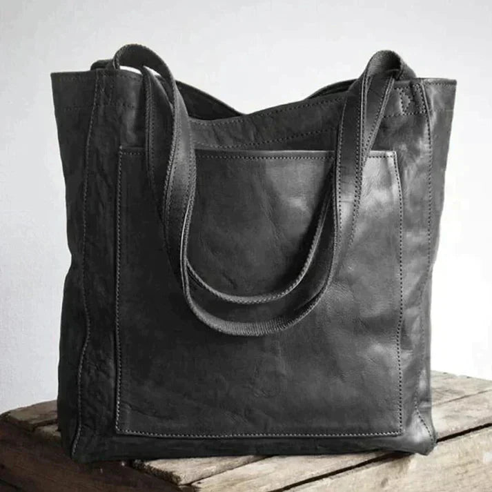 Sac à main en cuir noir élégant sur une table en bois, design moderne avec anses robustes. Accessoire mode femme, tendance et pratique.
