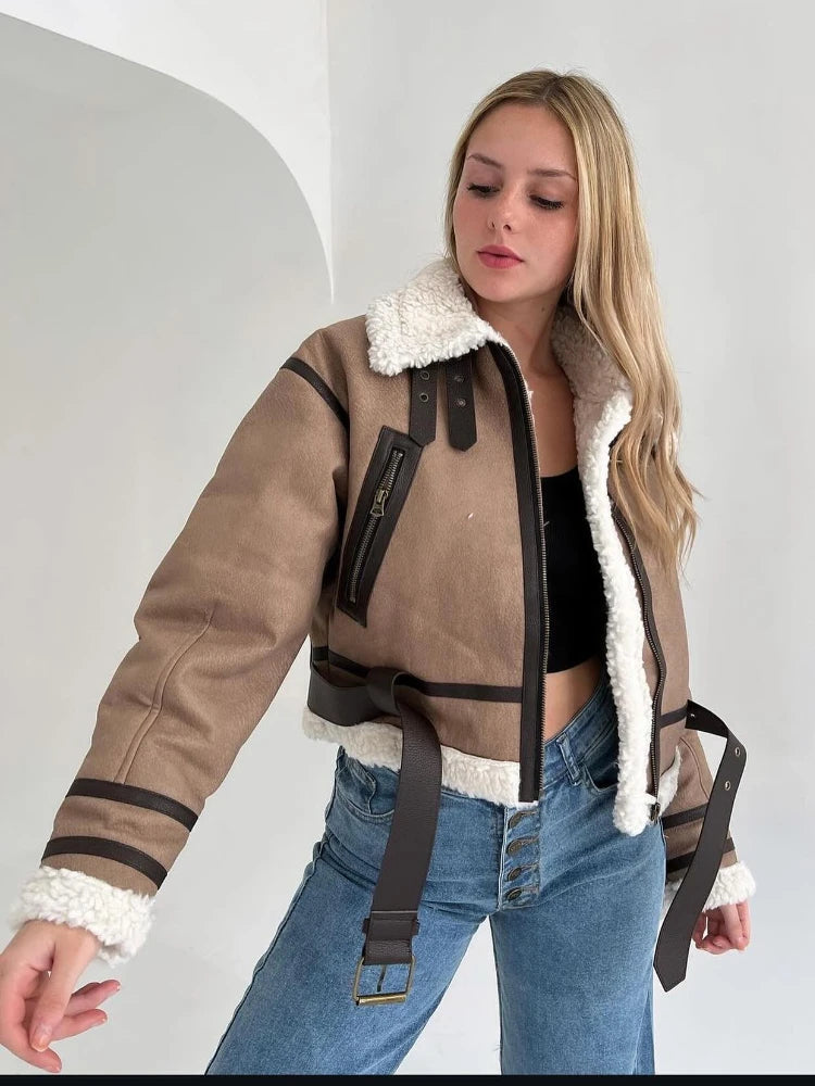 Jeune femme portant un blouson aviateur marron avec doublure en fourrure blanche, poches zippées, ceinture, et un jean bleu. Mode automne-hiver tendance.