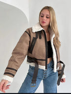 Jeune femme portant un blouson aviateur marron avec doublure en fourrure blanche, poches zippées, ceinture, et un jean bleu. Mode automne-hiver tendance.