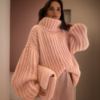 Femme portant un pull oversize rose en tricot à col roulé, manches bouffantes, dans un intérieur moderne. Mode hiver, tendance cosy.