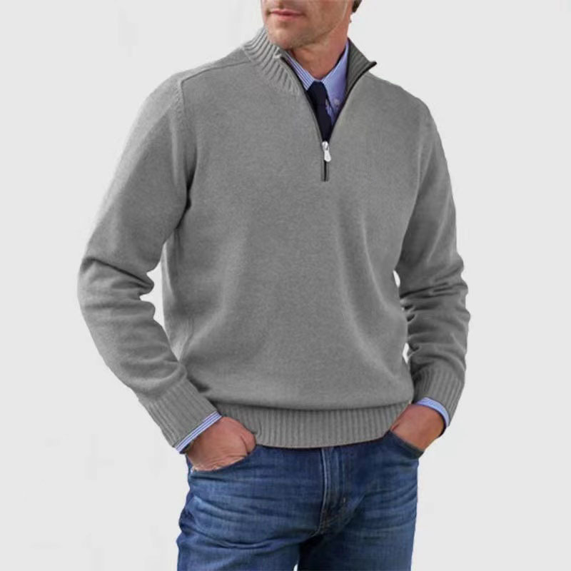 Homme portant un pull gris à col zippé, manches longues, sur une chemise bleue, avec un jean. Mode masculine élégante et décontractée.
