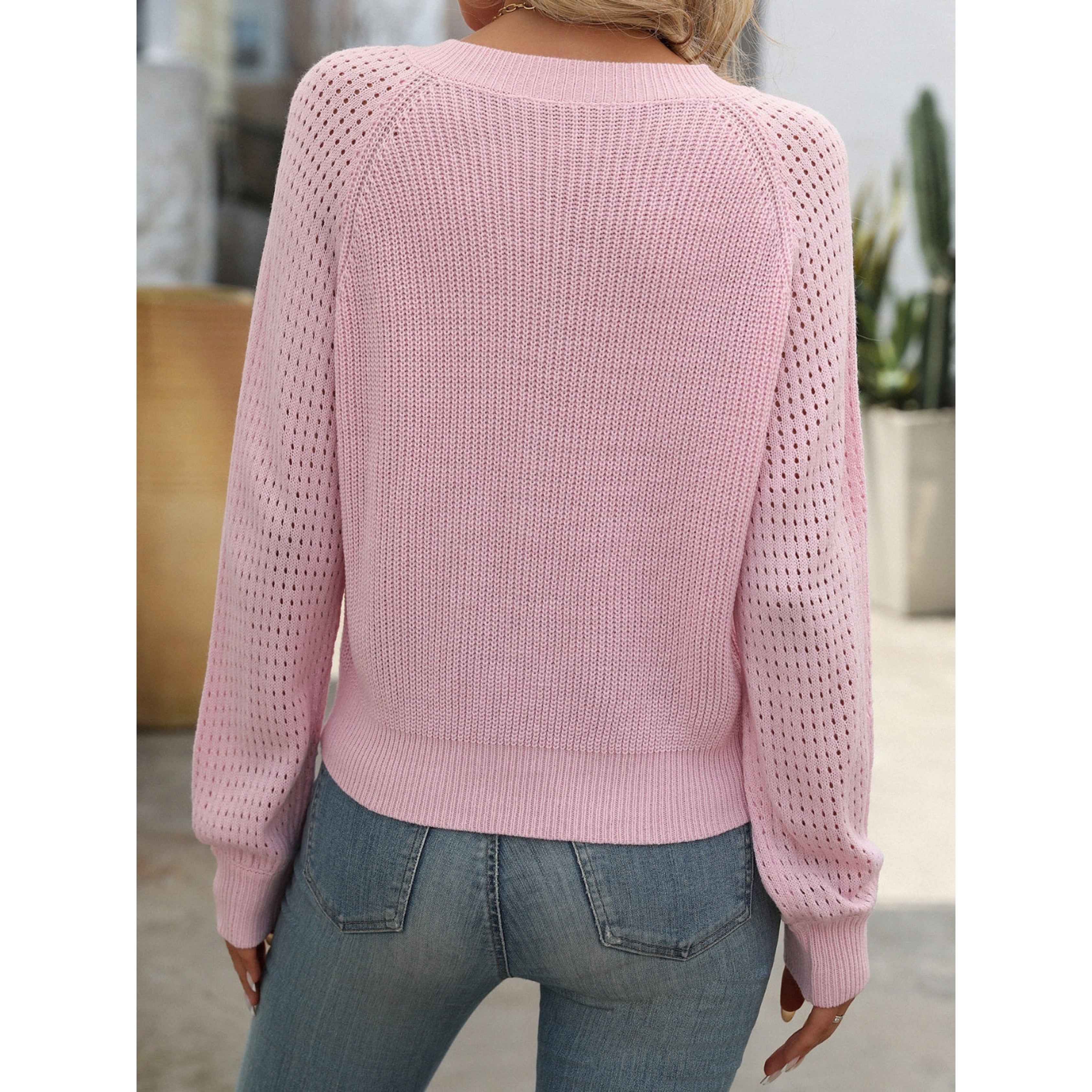 Femme portant un pull rose en maille ajourée, manches longues, dos visible, associé à un jean bleu. Mode féminine décontractée, tendance printemps.