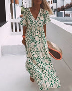 Robe longue à motifs floraux verts et blancs, femme marchant sur une terrasse en bois, style estival chic, accessoire sac en paille.