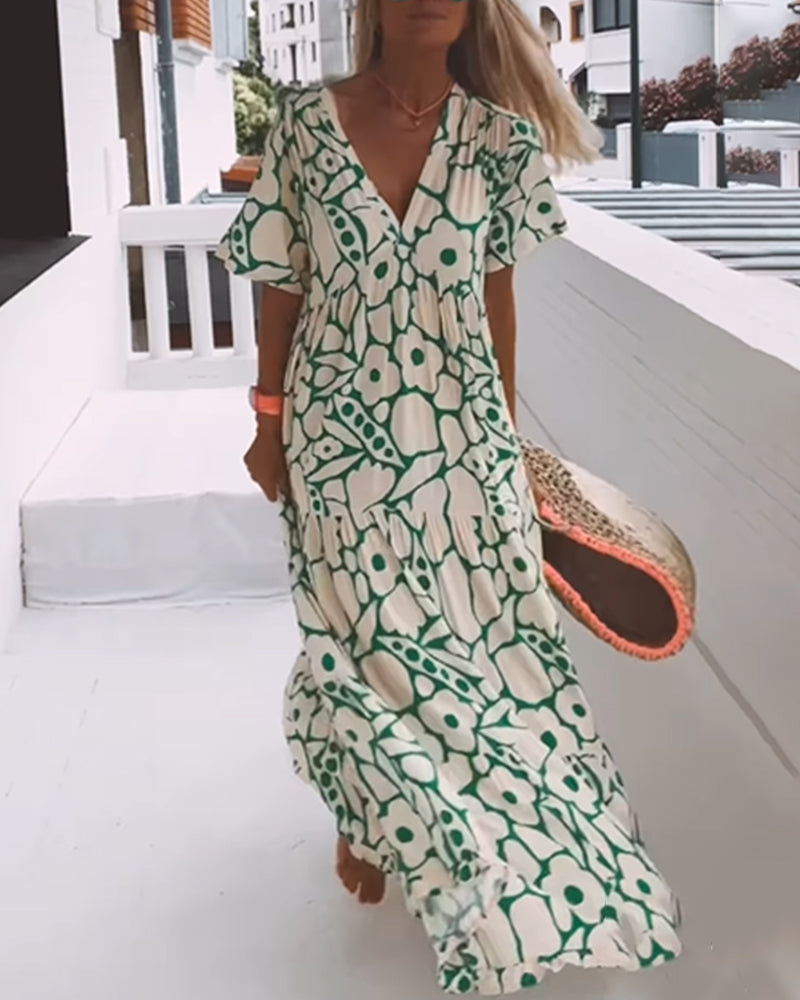 Robe longue à motifs floraux verts et blancs, femme marchant sur une terrasse en bois, style estival chic, accessoire sac en paille.