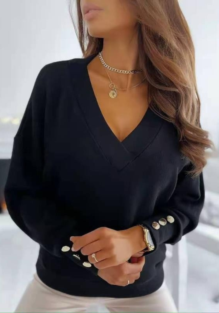 Femme portant un pull noir à col en V avec boutons dorés, collier chaîne et montre élégante. Mode automne chic, style décontracté tendance.