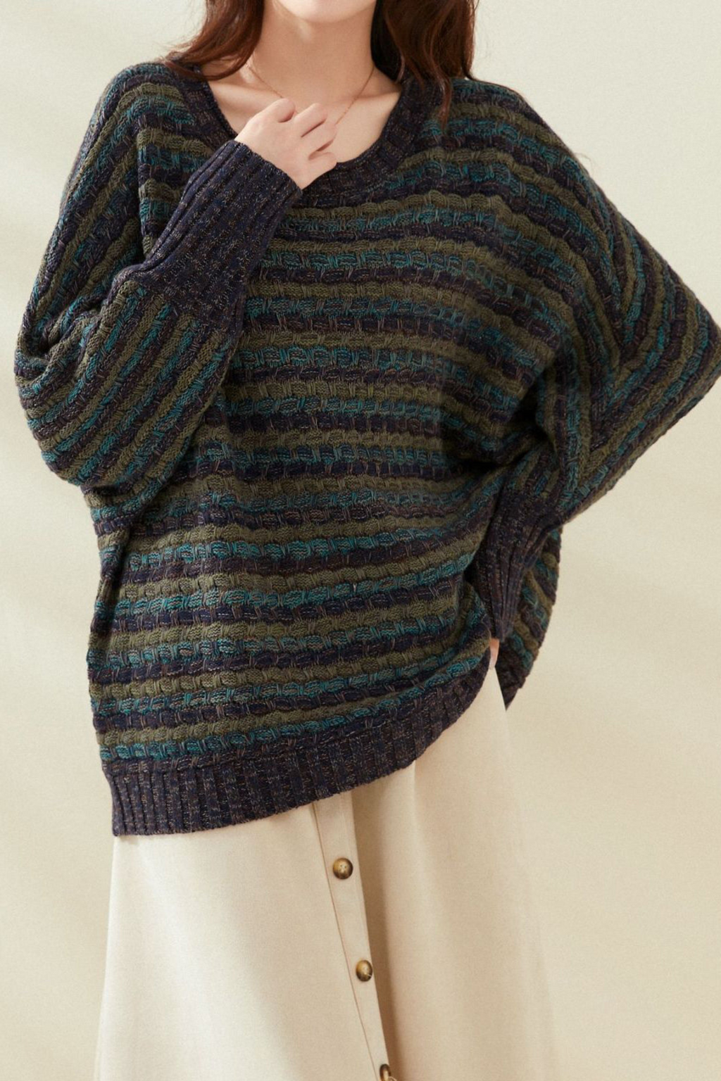 Femme portant un pull rayé bleu et vert, manches longues, sur une jupe beige à boutons. Mode automne-hiver, style décontracté et élégant.