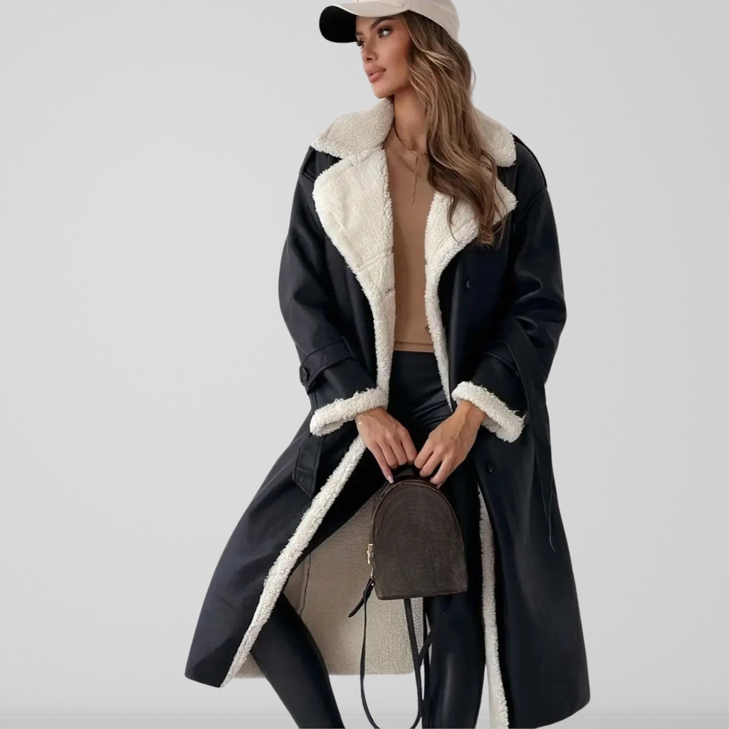 Femme portant un manteau long en cuir noir avec doublure en fourrure blanche, tenue chic avec pantalon noir, casquette beige et sac à dos marron.
