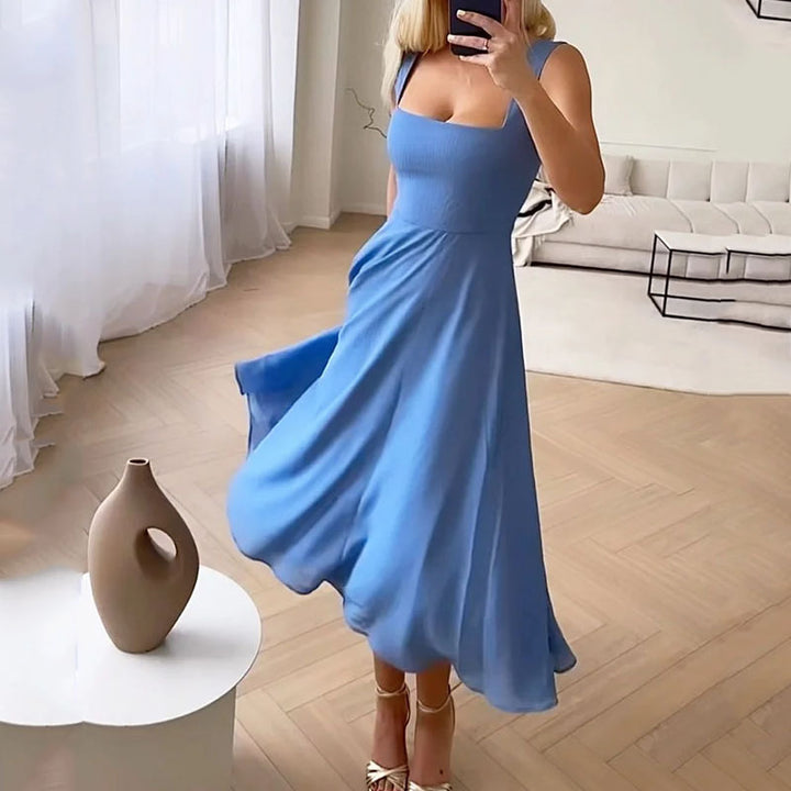 Robe bleue élégante portée par une femme dans un salon moderne, parquet en bois clair, vase décoratif, rideaux blancs, canapé minimaliste.