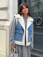 Femme portant une veste en jean doublée de fourrure, robe grise, tenant un sac à main élégant devant une porte en fer forgé. Mode automne chic.
