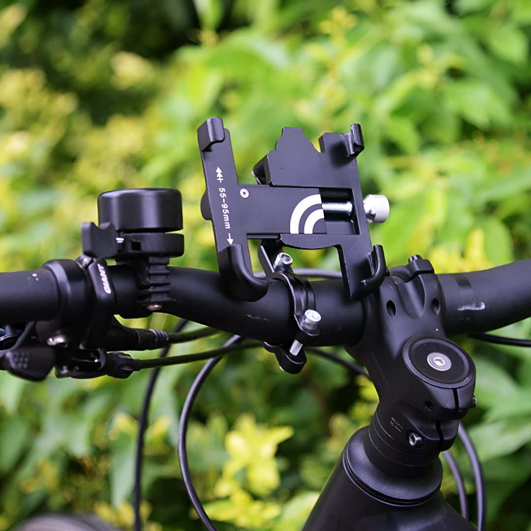 Support de téléphone pour vélo noir fixé sur un guidon, entouré de verdure. Accessoire pratique pour cyclistes, compatible avec divers modèles.