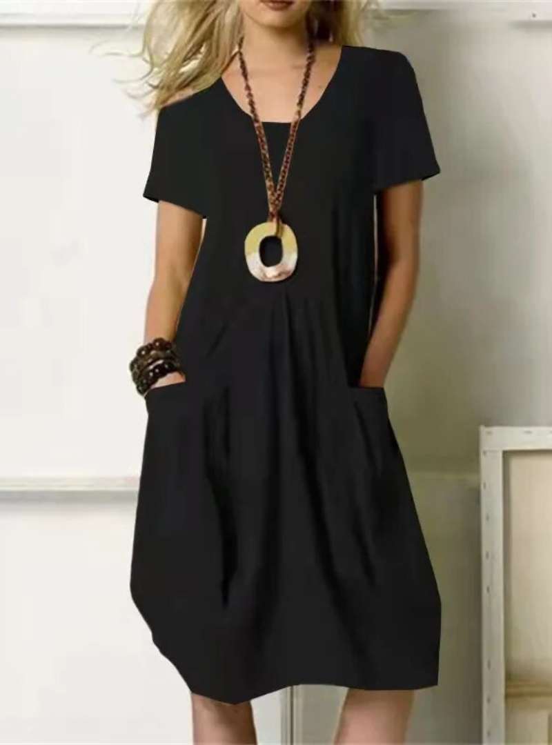 Robe noire élégante avec poches, collier pendentif ovale, manches courtes. Mode féminine chic, tenue décontractée, style moderne.