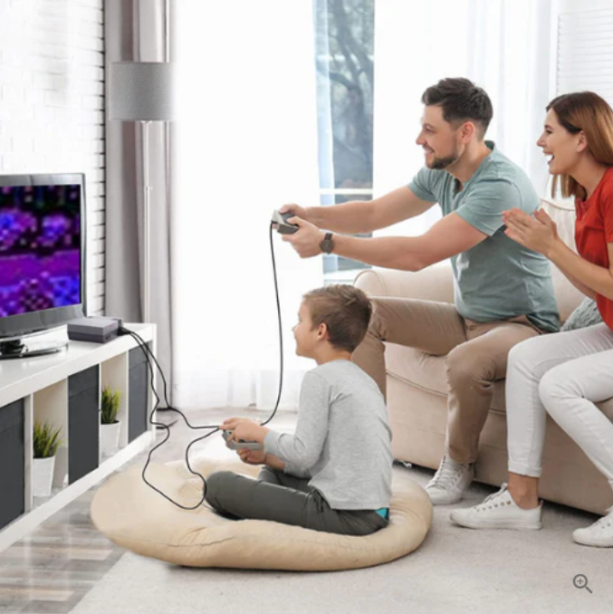 Famille jouant à un jeu vidéo rétro sur console classique, père et mère encouragent leur fils assis sur un coussin devant la télévision.