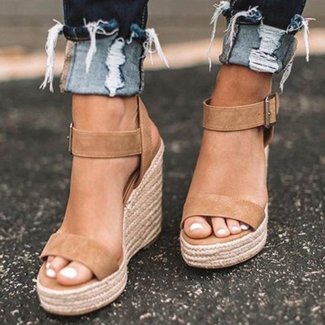 Sandales compensées en cuir beige sur pieds féminins, portées avec un jean déchiré. Mode estivale, chaussures tendance, style décontracté.