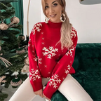 Femme souriante portant un pull rouge à motifs flocons de neige, assise près d'un sapin de Noël décoré. Mode hiver, tenue festive, ambiance Noël.