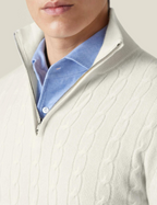 Homme portant un pull blanc à col zippé en maille torsadée sur une chemise bleue. Mode masculine élégante, style automne-hiver.