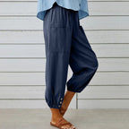 Pantalon ample bleu marine avec poches, boutons décoratifs aux chevilles, porté avec des sandales marron. Mode décontractée femme, tendance été.