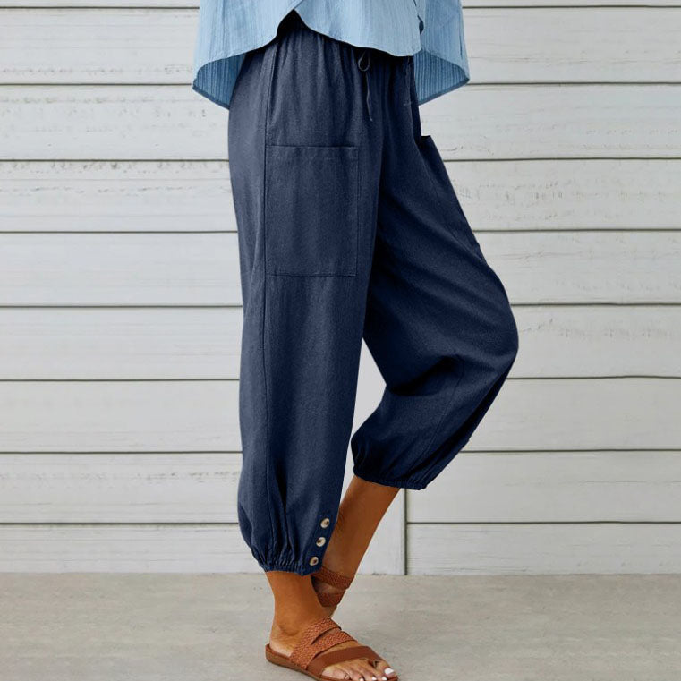 Pantalon ample bleu marine avec poches, boutons décoratifs aux chevilles, porté avec des sandales marron. Mode décontractée femme, tendance été.