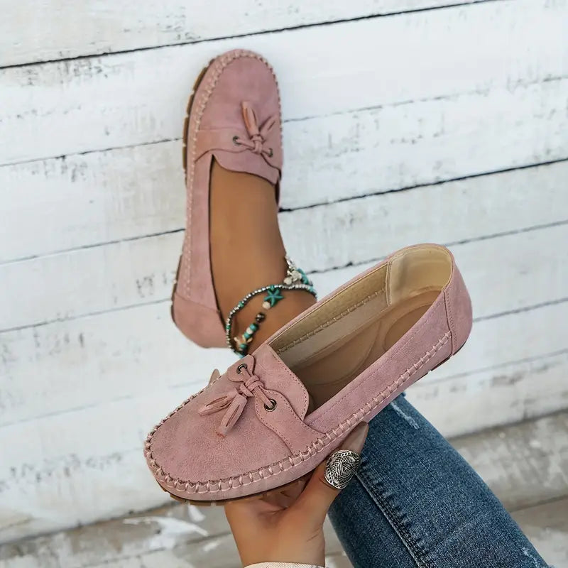 Mocassins roses en daim pour femme, ornés d'un nœud, portés avec un jean. Chaussures élégantes et confortables, tendance mode féminine.