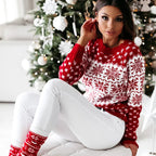 Femme en pull rouge à motifs flocons de neige, assise devant un sapin de Noël décoré. Mode hiver, ambiance festive, tenue de Noël élégante.