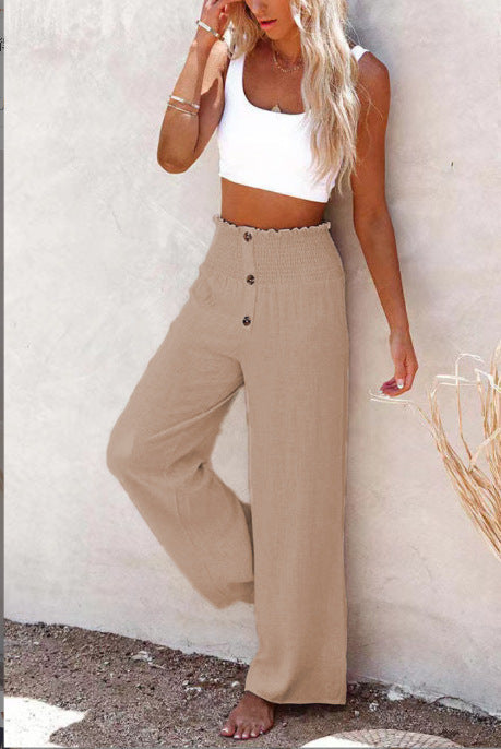 Femme en top blanc et pantalon beige taille haute, posant contre un mur. Mode estivale, tenue décontractée, style chic et tendance.