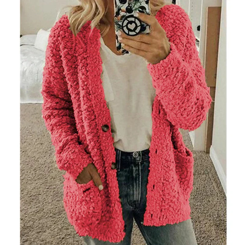 Femme portant un cardigan rose en tricot texturé, t-shirt blanc et jean, tenant un smartphone. Mode automne-hiver, style décontracté.