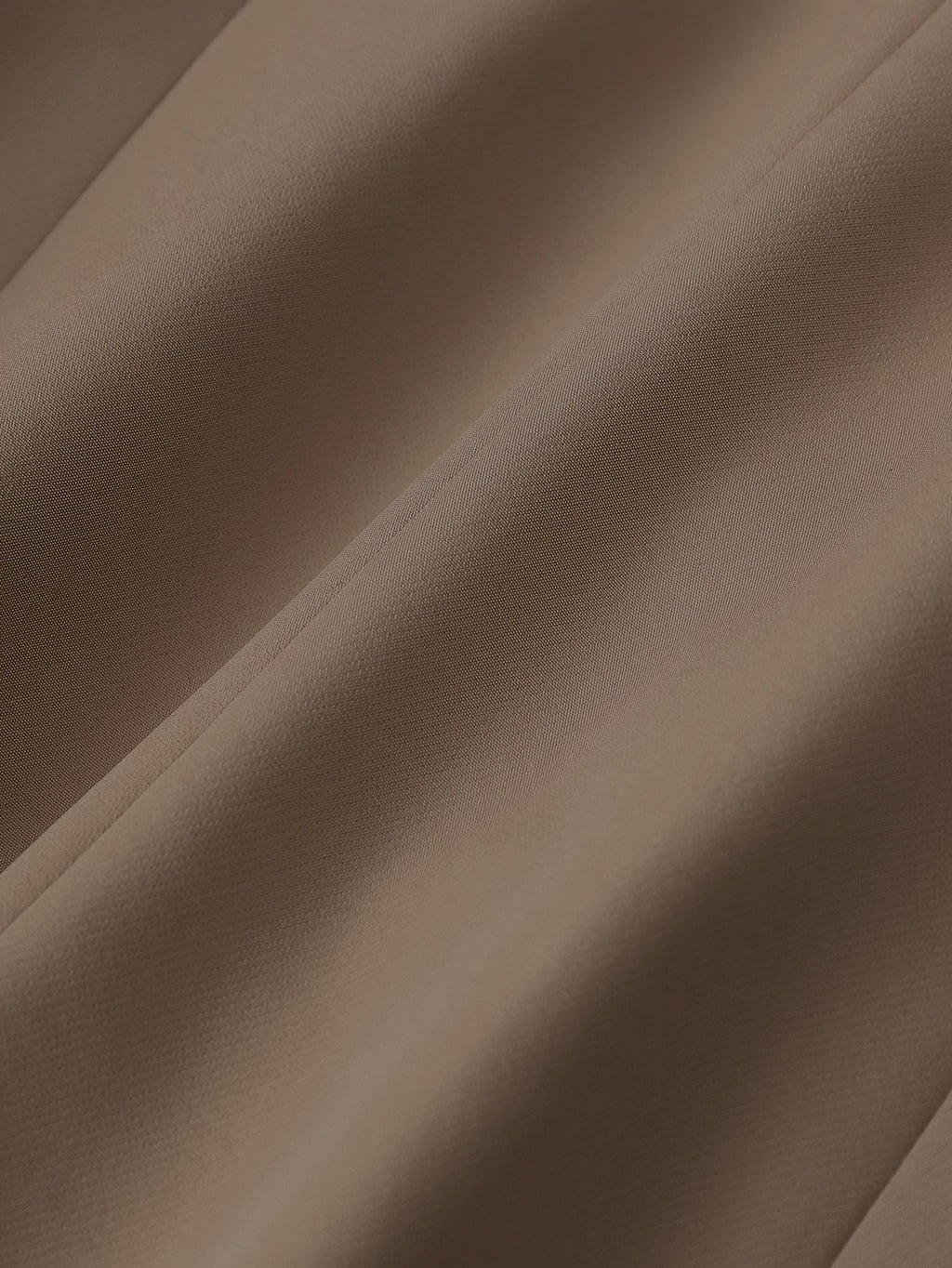 Tissu marron en gros plan, texture douce et plissée, textile élégant pour mode et décoration intérieure, fond neutre et chaleureux.