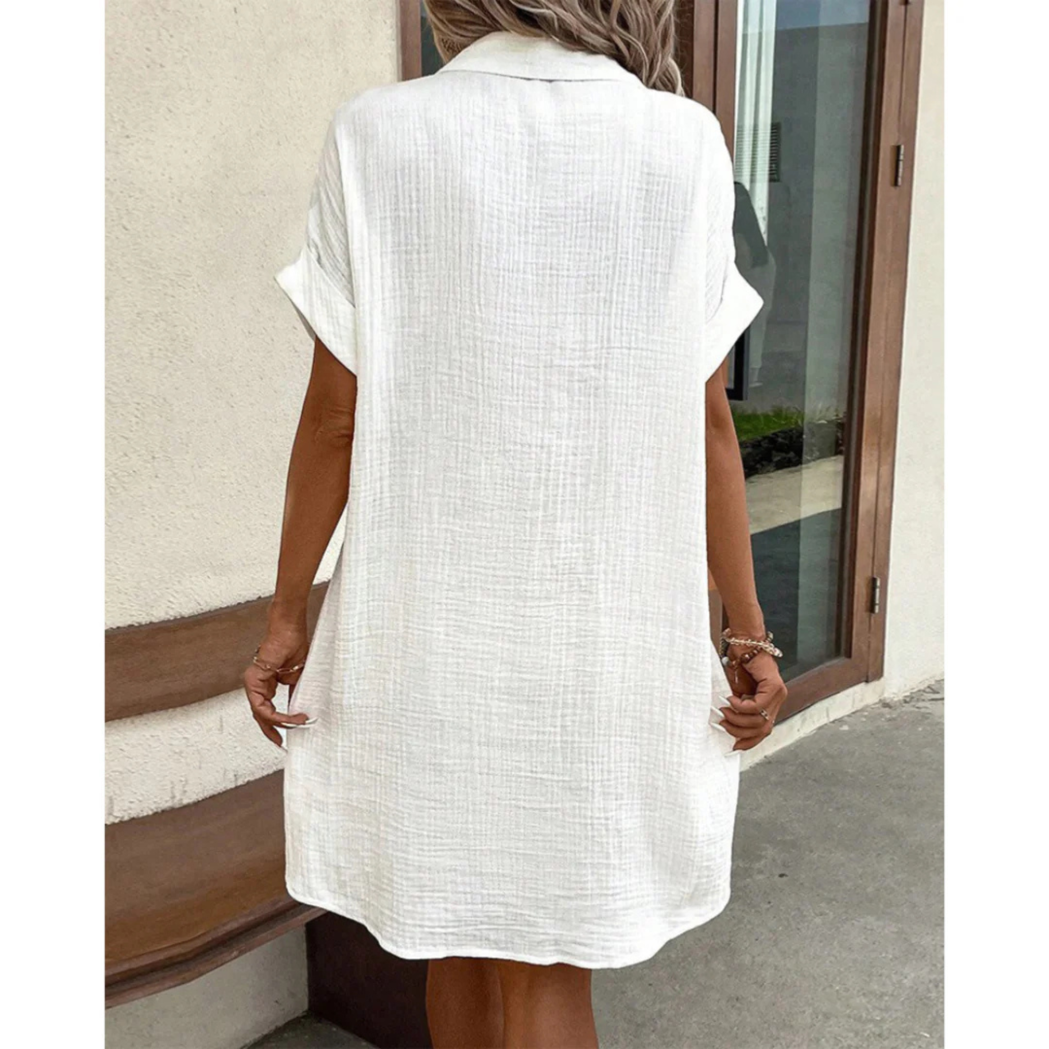 Robe chemise blanche en lin pour femme, manches courtes, style décontracté, devant une porte en bois. Mode estivale élégante et confortable.
