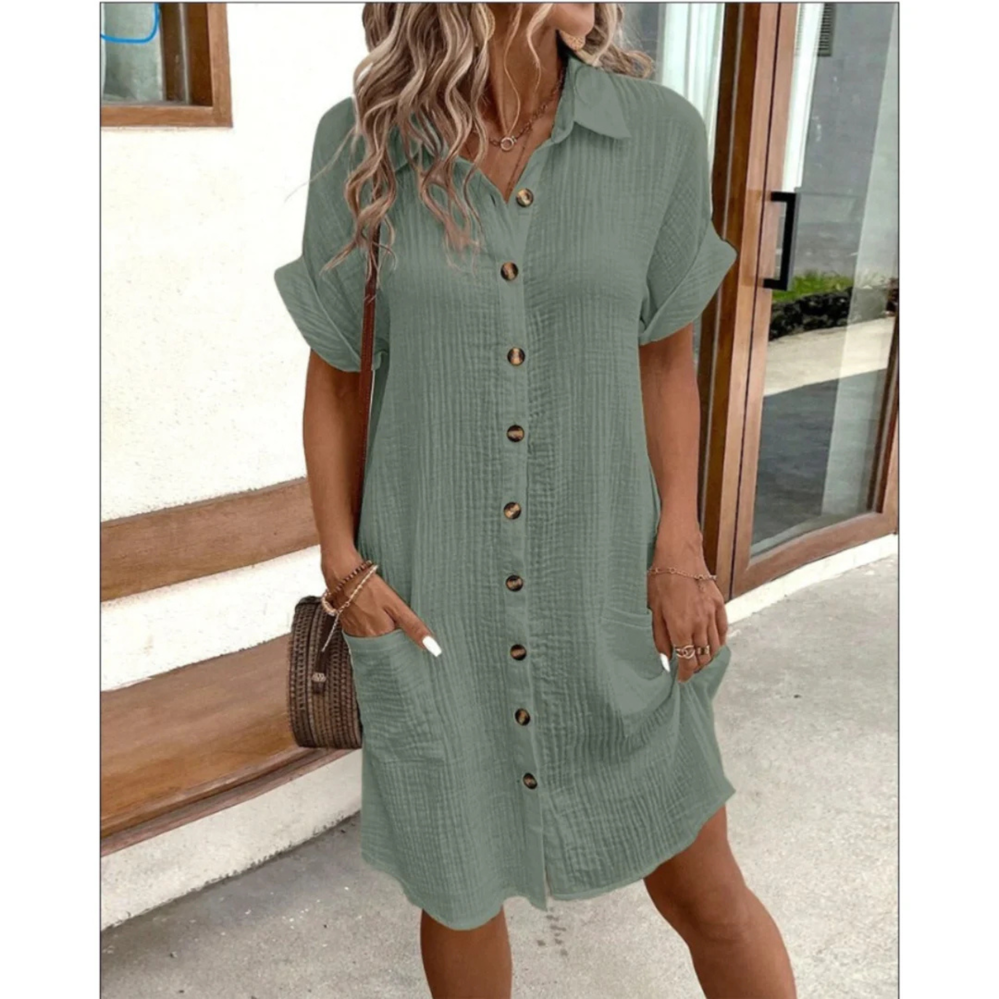 Robe chemise verte à manches courtes avec boutons en bois, poches latérales, portée par une femme aux cheveux ondulés, devant un mur blanc.