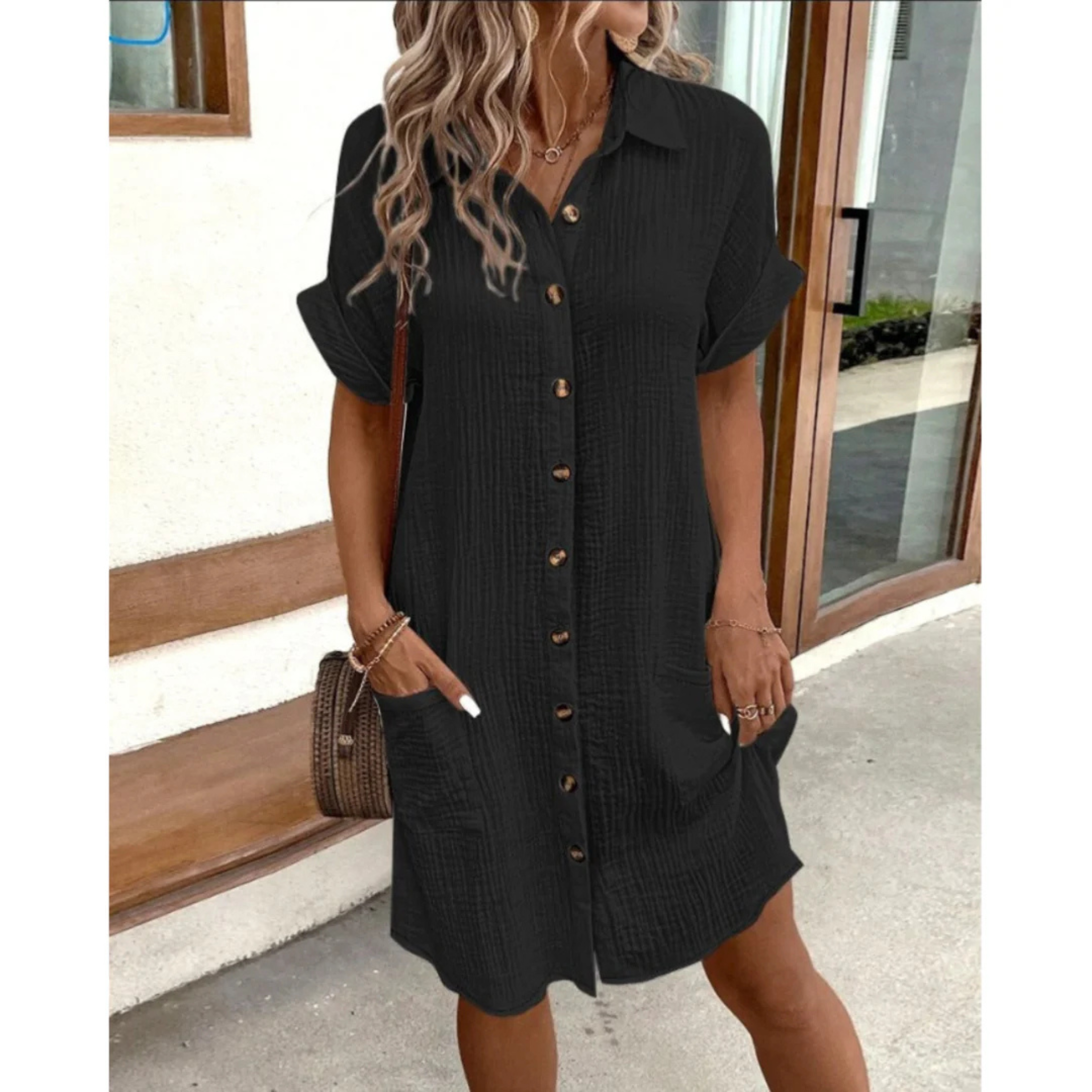 Robe chemise noire à manches courtes, boutons en bois, poches latérales, portée par une femme blonde. Mode décontractée, tendance été.