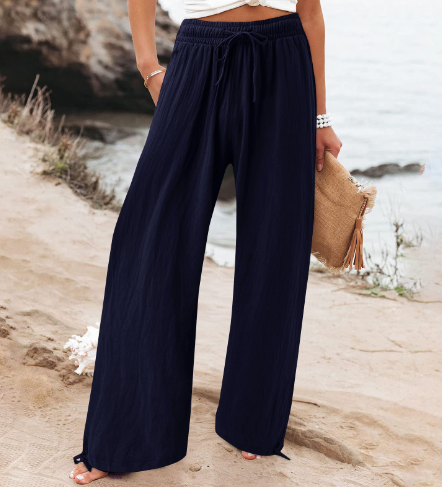 Pantalon large bleu marine pour femme, style décontracté, bord de mer, accessoire sac en paille, mode estivale, plage, confort et élégance.
