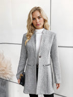 Femme blonde portant un manteau gris élégant, debout devant un mur blanc. Mode automne, style chic, tenue professionnelle.