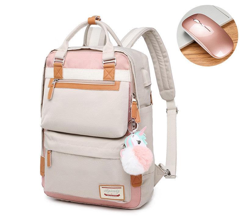 Sac à dos beige et rose avec pompon licorne, poches multiples, détails en cuir marron, accompagné d'une souris sans fil rose sur bureau en bois.