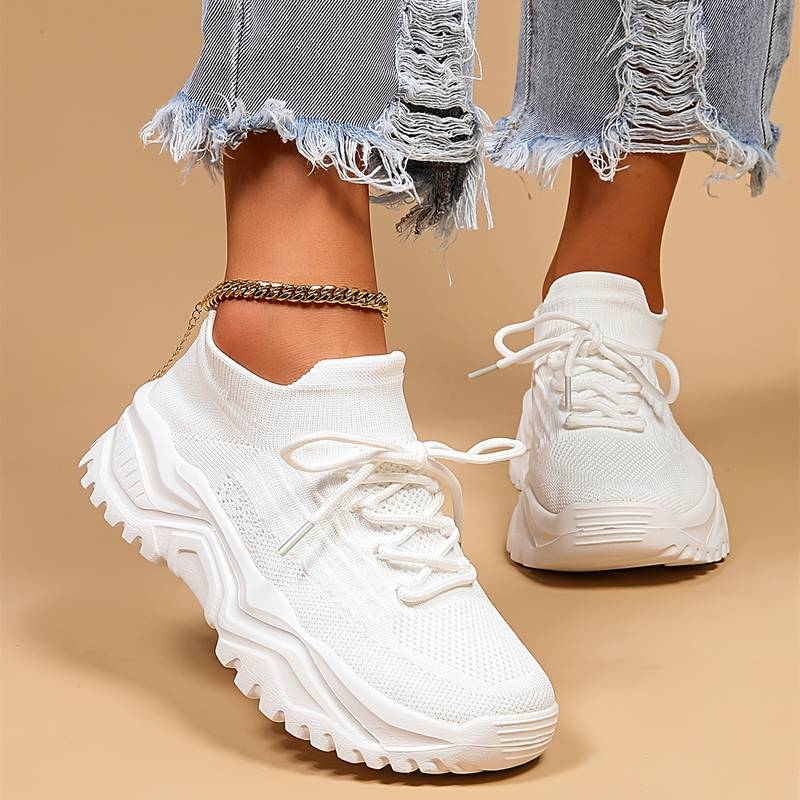 Baskets blanches tendance avec semelle épaisse, portées avec un jean déchiré. Chaussures de sport modernes pour un look décontracté et stylé.