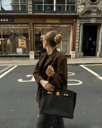Femme élégante avec chignon, portant un sac à main noir de luxe, devant une boutique de mode. Style chic, mode urbaine, accessoires haut de gamme.