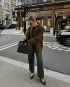 Femme élégante portant un manteau marron et un sac à main noir devant une boutique Delvaux à Londres, rue animée avec taxis et piétons.