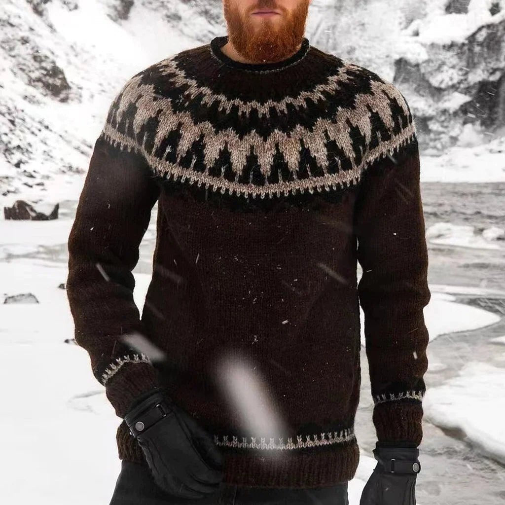 Homme barbu portant un pull en laine islandais noir avec motifs traditionnels, debout dans un paysage enneigé. Mode hiver, vêtements chauds.