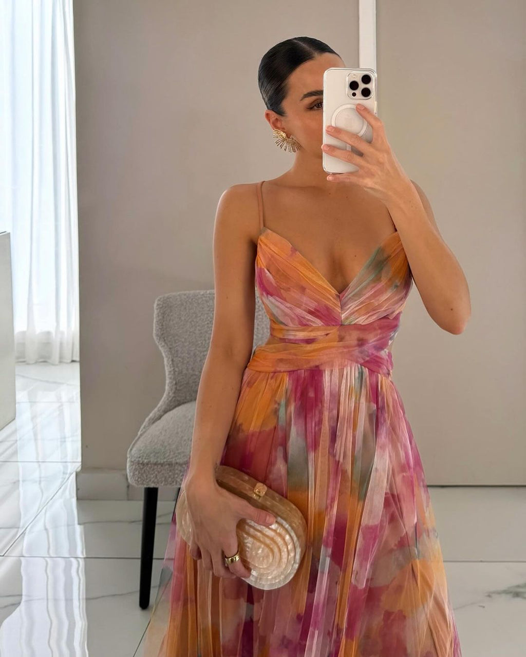 Femme en robe longue colorée, tenant un sac à main nacré, se prenant en photo devant un miroir. Mode élégante, tenue de soirée chic.