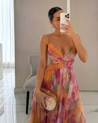 Femme en robe longue colorée, tenant un sac à main nacré, se prenant en photo devant un miroir. Mode élégante, tenue de soirée chic.