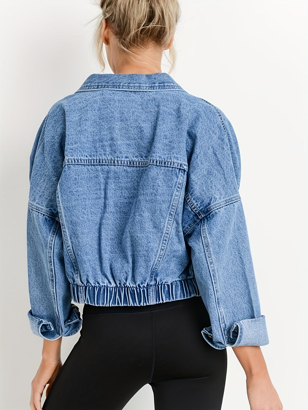 Femme portant une veste en jean bleu oversize avec manches retroussées, vue de dos. Mode décontractée, tendance denim, style urbain.