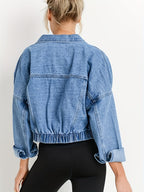 Femme portant une veste en jean bleu oversize avec manches retroussées, vue de dos. Mode décontractée, tendance denim, style urbain.