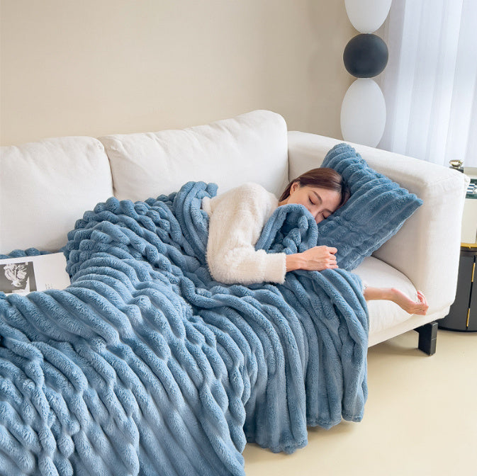 Femme dormant sur un canapé blanc, enveloppée dans une couverture en fausse fourrure bleue. Décoration intérieure moderne, ambiance cosy et relaxante.