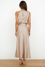 Robe longue en satin beige, sans manches, col haut, vue de dos, portée par une femme. Mode élégante, tenue de soirée chic, style moderne.