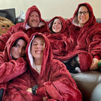 Cinq personnes souriantes portant des couvertures à capuche rouges, assises sur un canapé. Ambiance chaleureuse et conviviale.