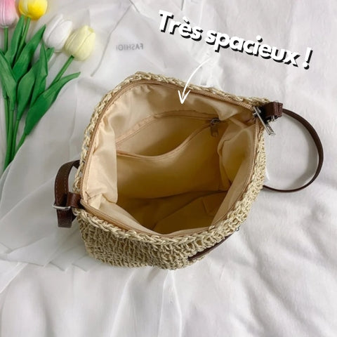 Sac en paille tressée ouvert, intérieur spacieux avec poche zippée, bandoulière marron, posé sur tissu blanc, tulipes colorées à côté.